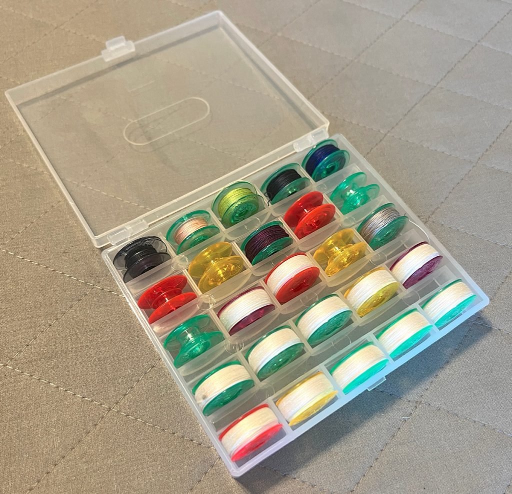 Clear plastic box of bobbins with hinged lid