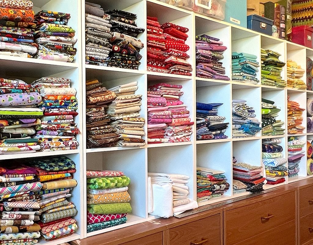 Wall of colorful folded fabrics in cube shelves, sorted by color.