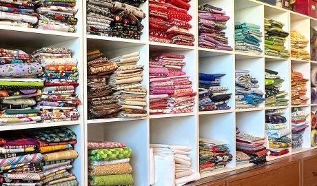 Wall of colorful folded fabrics in cube shelves, sorted by color.