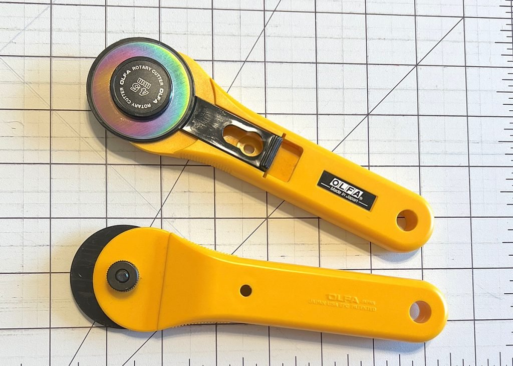 Two yellow rotary cutters, one upside down, on a white gridded cutting surface